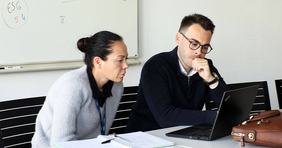 Un homme et une femme sont assis autour d'une table, engagés dans une conversation, probablement liée aux informations affichées sur l'ordinateur portable. 